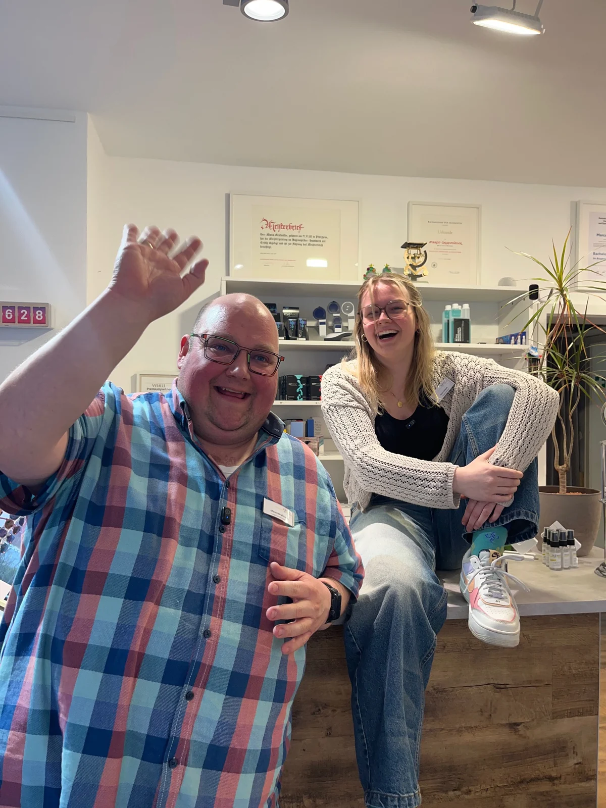 Marco Grafmüller winkt, Nina Siebert sitzt lachend auf dem Tresen bei Optik Schenk